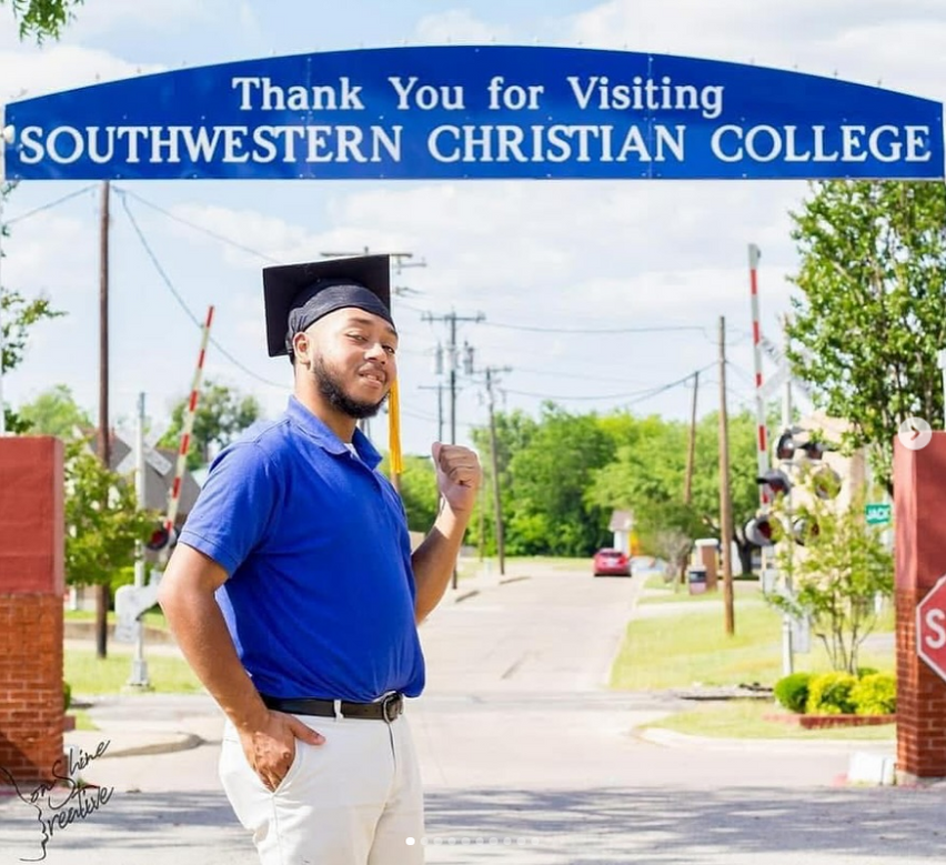 A graduate poses at the Southwestern Christian College entrance sign